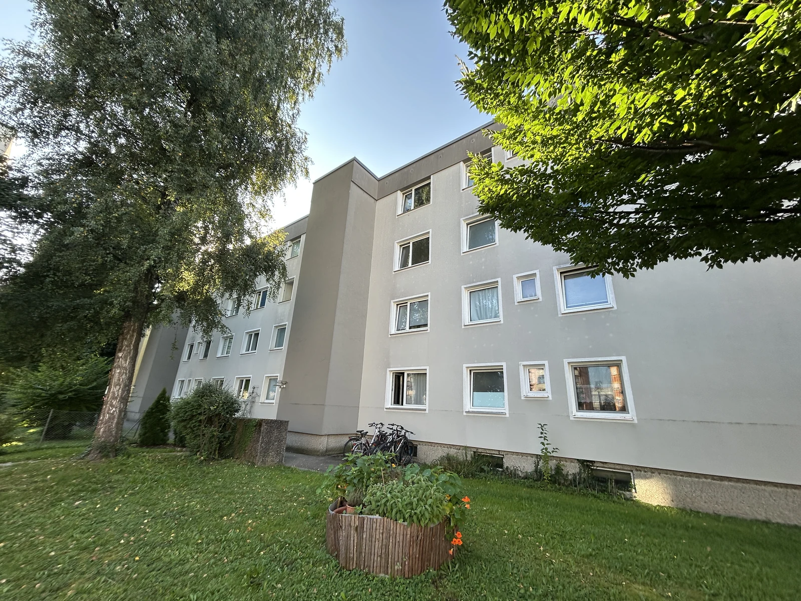 Mehrgeschossige Putzfassade eines Mehrfamilienhauses mit unterschiedlich großen Fenstern und Kellerfenstern